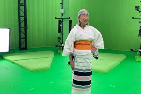 a woman dressed in Japanese kimono and headband stands in a green room filled with lights and cameras