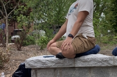 A man sits on a stone ledge, his legs crossed in a yoga position. Monday Meditation with GT Meditation Club.